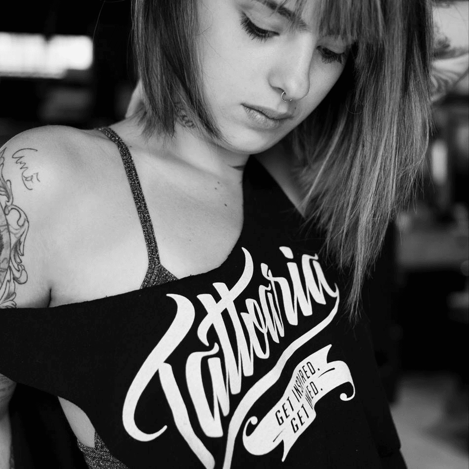 Foto em preto e branco: mulher tatuada vestindo a regata preta da Tattoaria caída no ombro.